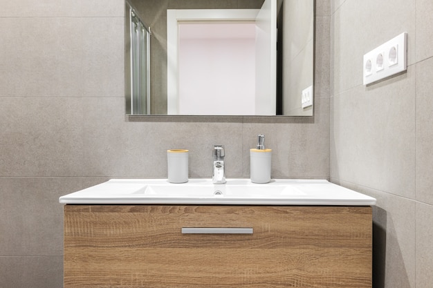 改装されたバスルームにモダンな木製ベースと鏡付きの白いシンク