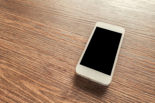 木製の机の上に空白の画面を持つ白いスマートフォン