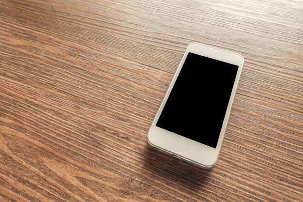 Белый смартфон с пустым экраном на деревянном столе