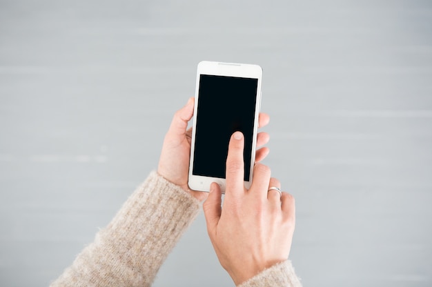Бесплатное фото Белый смартфон в женских руках на сером фоне