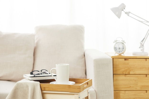 Бесплатное фото Белый диван с маленькими столиками возле него с лампой, будильником и личными вещами на них