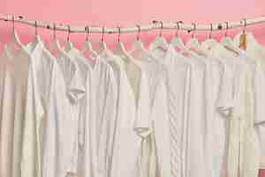 Free photo white solid clothes hanging in one row on wooden racks against pink background. big choice for women in retail shop.