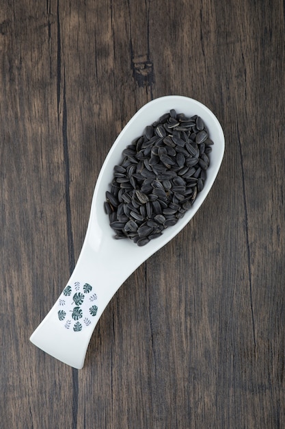 Free photo white spoon full of healthy black sunflower seeds placed on a wooden table .