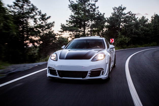 A white sport car with black autotuning driving on the road.