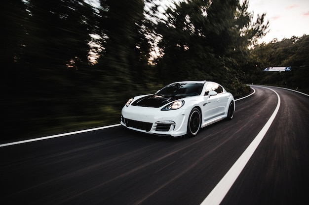 A white sport car with black autotuning driving with high speed on the road.