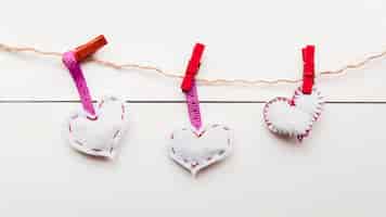 Free photo white stitch hearts on rope tied with red clothespins on string against wooden plank