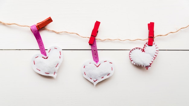 White stitch hearts on rope tied with red clothespins on string against wooden plank