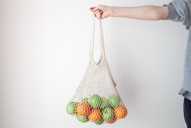 Free photo white string bag with fruits on a white background
