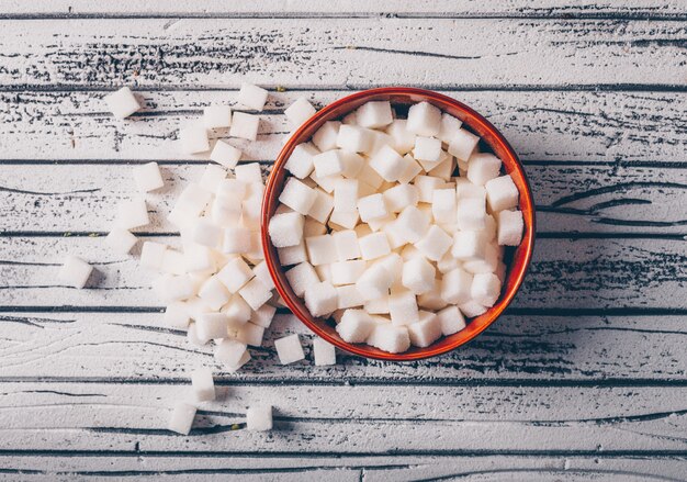 White sugar cubes in a bowl on a white wooden table. top view.