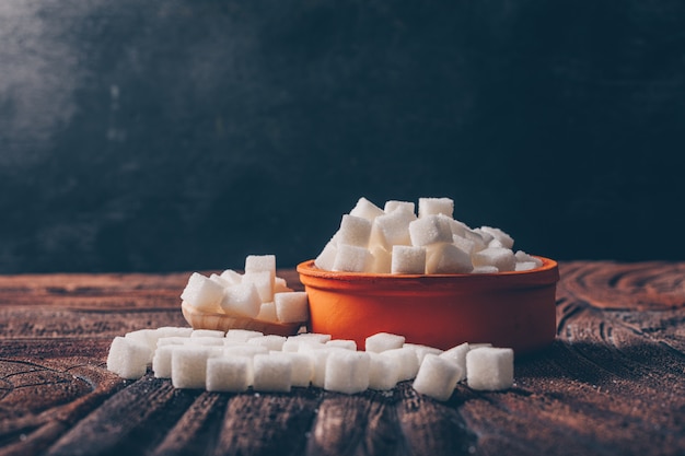White sugar cubes in a orange bowl with spoon side view on a dark and wooden table