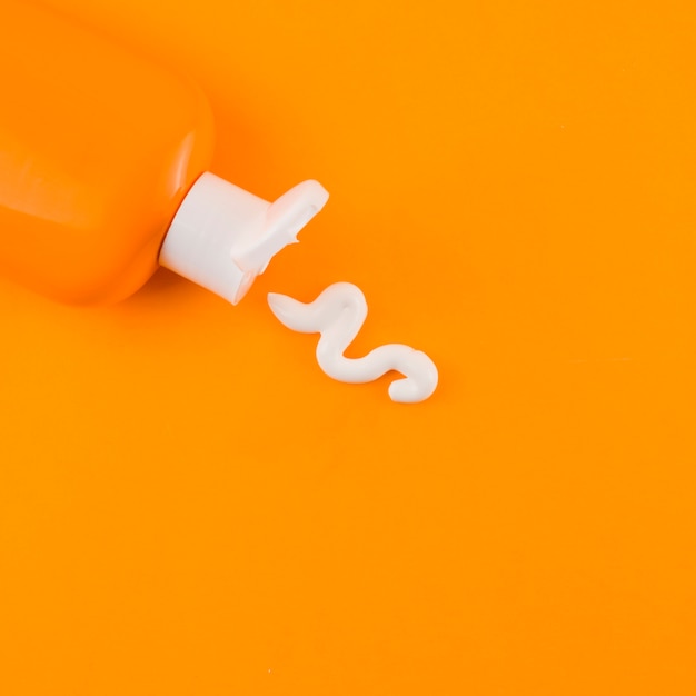 Белый солнцезащитный крем из оранжевой бутылки на оранжевом фоне