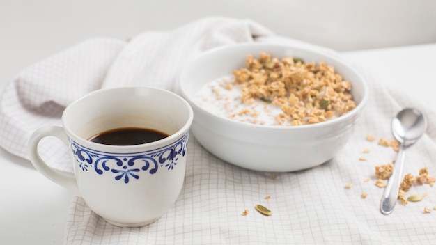White tea cup; bowl of oatmeal porridge on tablecloth