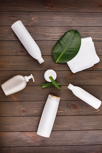 白いタオル、シャンプーとコンディショナーのボトルは、緑の葉とアロエとテーブルの上に横たわっています