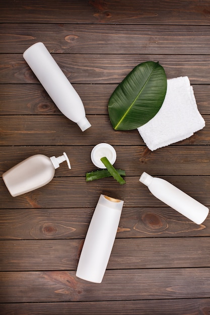 White towel, bottles of shampoo and conditioner lie on a table with green leaf and aloe