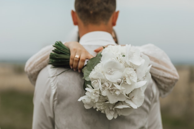 White wedding bouquet made of callas and a woman is hugging a man outdoors