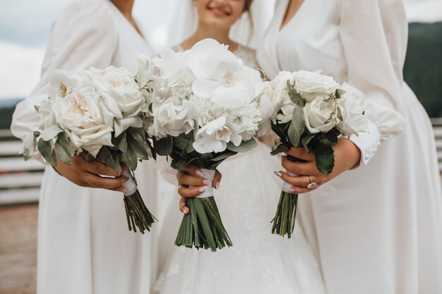 White wedding bouquets for bride and bridesmaids made of callas and orchids in hands outdoors