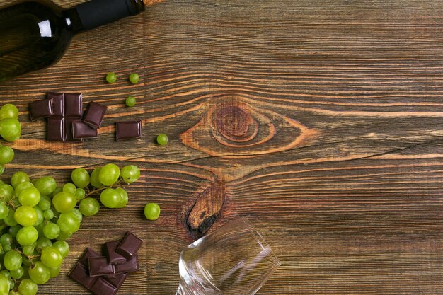 복사 공간이 있는 나무 탁자 위의 화이트 와인 병 포도 초콜릿과 안경 프리미엄 사진
