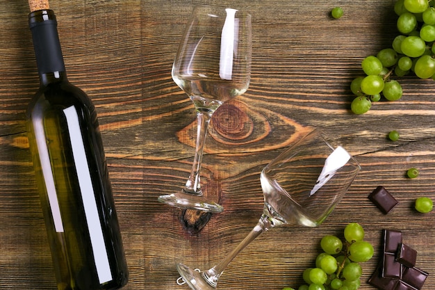 コピースペースと木製のテーブルトップビューの上の白ワインボトルグレープチョコレートとグラス