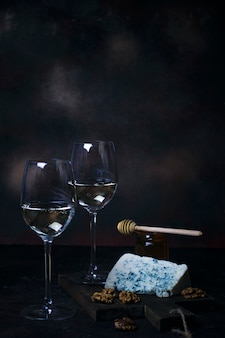 White wine in fine glass with blue cheese, honey, walnuts on dark