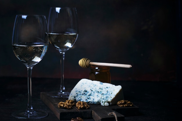 White wine in fine glass with blue cheese, honey, walnuts on dark 