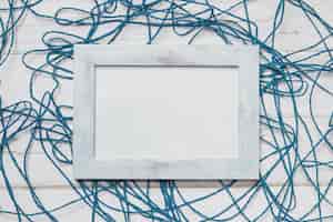 Free photo white wooden surface with blue rope and blank frame