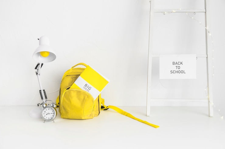 Free Photo white workplace for pupil with yellow bag and alarm clock