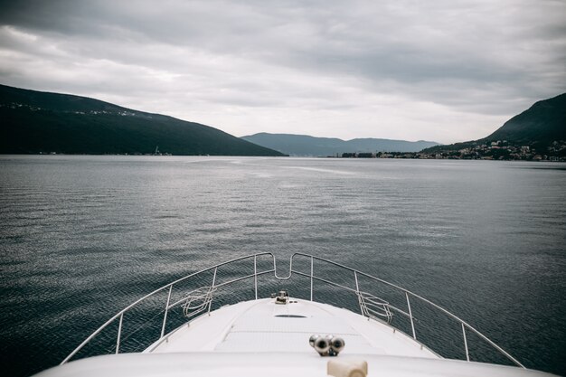 White yacht crosses sea leaving mountains with fog behind it