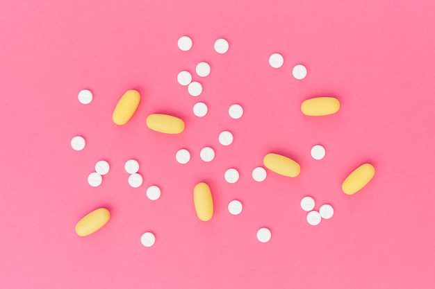 White and yellow medical pills on pink background