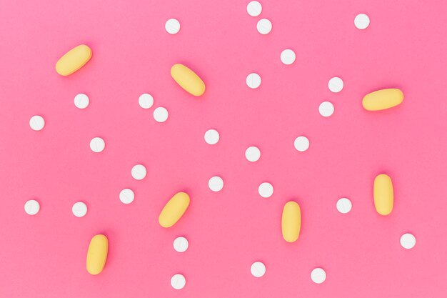 White and yellow pills on pink background