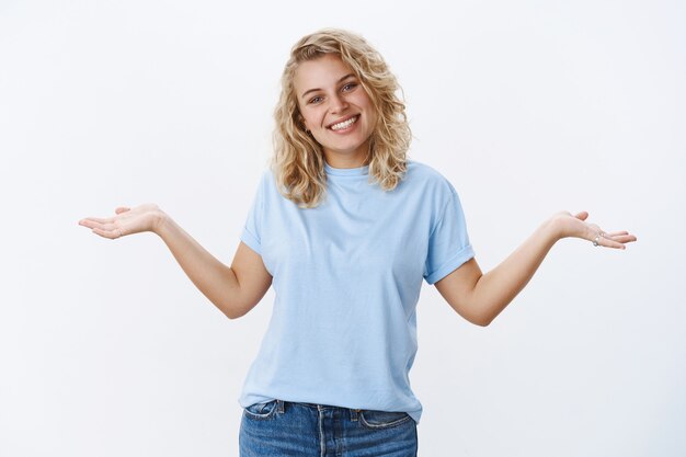 Who cares chill and be happy. Portrait of charismatic carefree young 25s girl with blue eyes tilting head joyfully as shrugging unaware and unbothered, spread hands sideways in clueless gesture