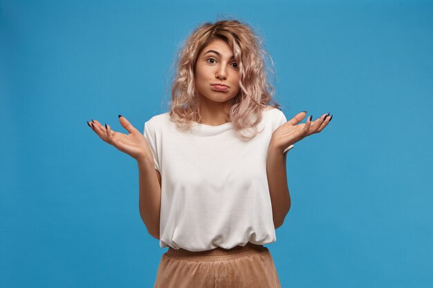 Free photo who cares, i don't know, not my problem. portrait of stylish young european female wearing beige skirt and white top shrugging shoulders