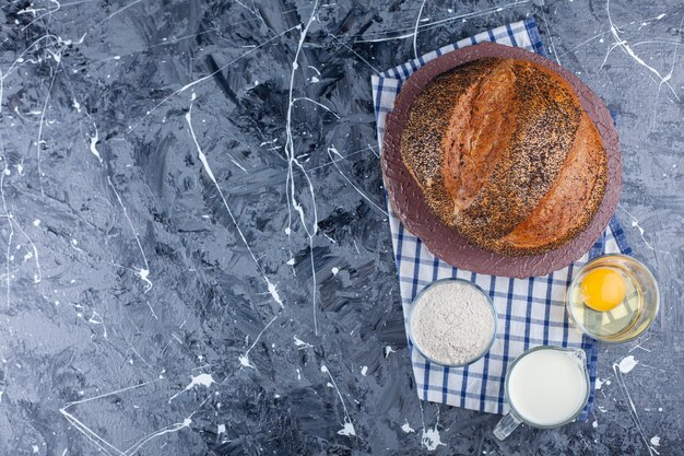 Whole bread, egg, flour and milk on a tea towel , on the blue background.