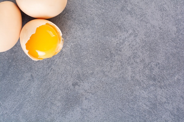 Whole and broken raw chicken eggs on stone table.