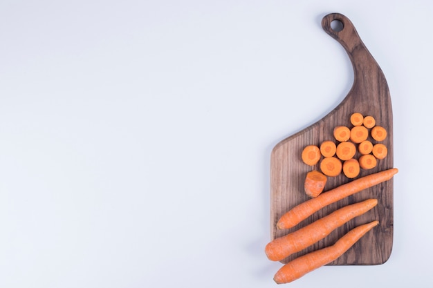 Whole and chopped carrots on a wooden board.