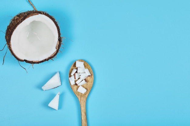 Whole coconut and pieces of coconut on wooden spoon.