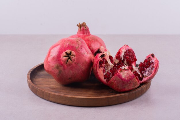 Whole and cut pomegranates on wooden plate.