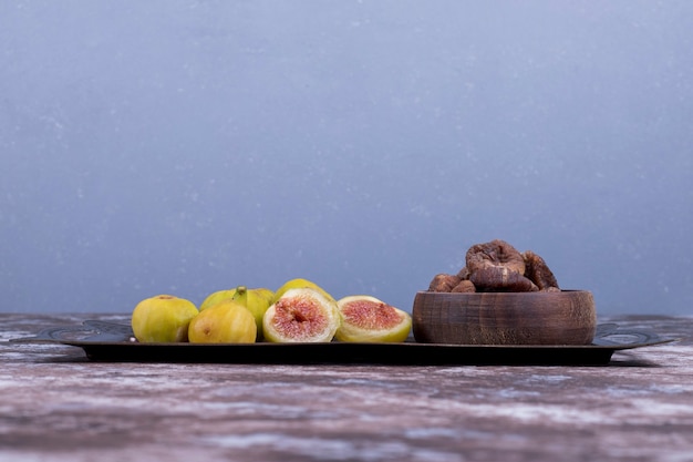 Free photo whole, dry and sliced figs in a metallic tray and in a wooden cup on blue.