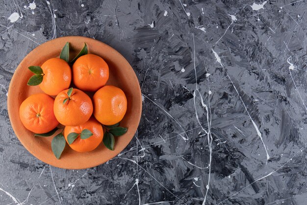 Whole fresh orange fruits with leaves placed in clay plate.