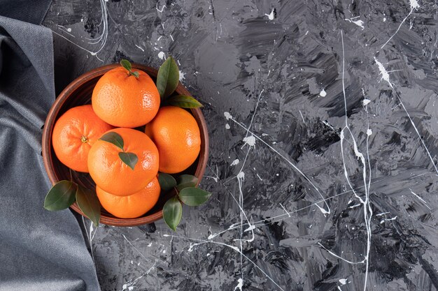 Whole fresh orange fruits with leaves placed on wooden bowl