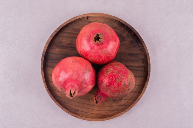 Whole fresh pomegranates on wooden plate.