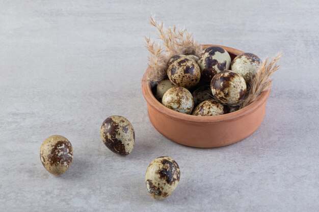 Whole fresh raw quail eggs with wheat ears placed on stone table. 