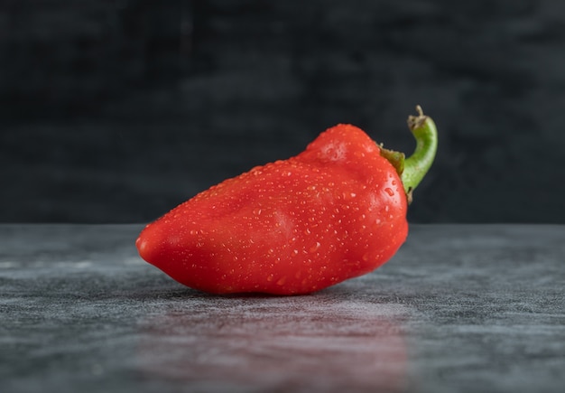 A whole fresh red pepper on a marble surface.