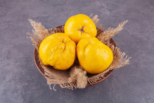 Whole fresh ripe quince fruits placed in a bowl with sackcloth . 