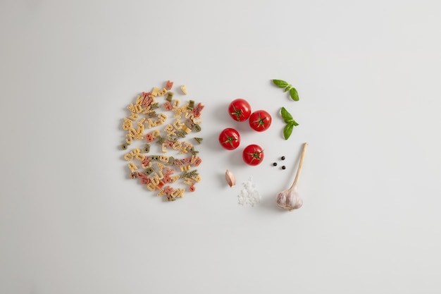 Whole grain colorful pasta with letter shape isolated on white background with tomatoes, sea salt, garlic, peppercorns, high in crabs. Healthy toppings for your pasta such as vegetables, fats, protein