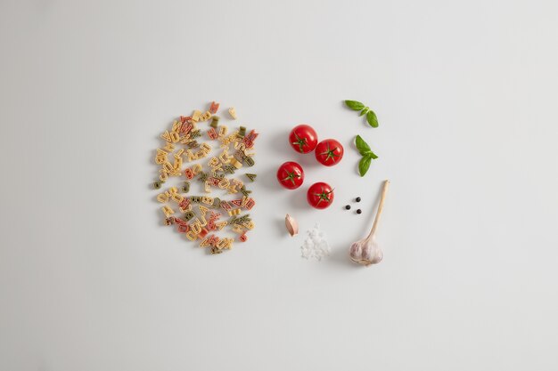 Whole grain colorful pasta with letter shape isolated on white background with tomatoes, sea salt, garlic, peppercorns, high in crabs. Healthy toppings for your pasta such as vegetables, fats, protein