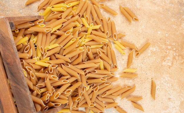 Whole grain penne pasta in a overturned wooden box , on the marble.