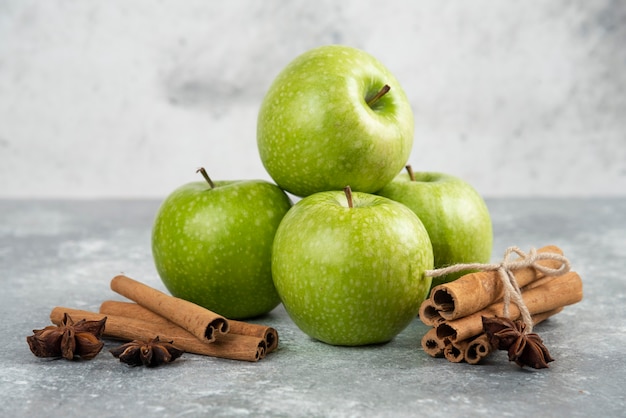 Whole green apples and cinnamon sticks on marble table.