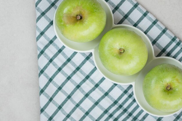 Целые зеленые яблоки на белых тарелках с полосатой скатертью
