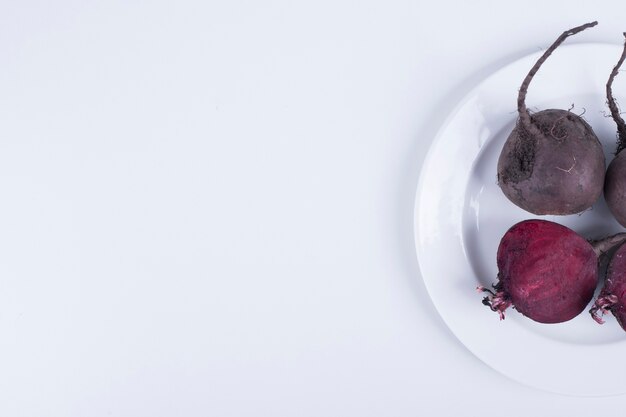 Whole and half beetroots in a white plate on right side.