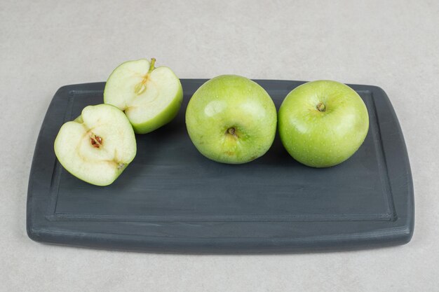 Целые и пополам нарезанные зеленые яблоки на темной тарелке